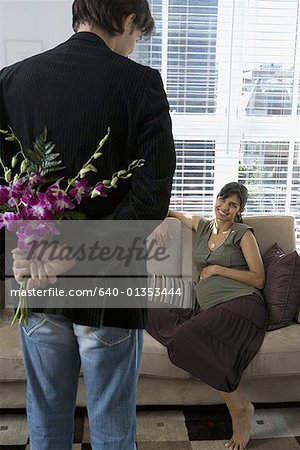 Rear view of a man holding flowers and looking at a pregnant woman