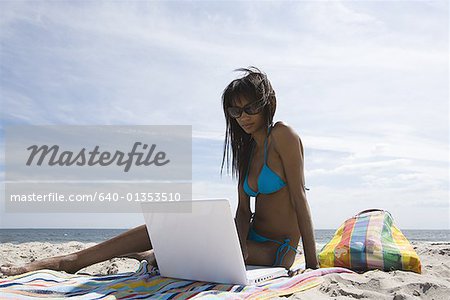 Vue d'angle faible d'une jeune femme à l'aide d'un ordinateur portable sur la plage