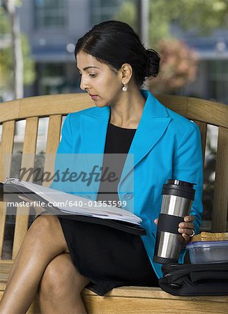 Businesswoman sitting on a bench and reading documents in a coffee break