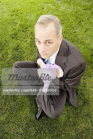 High angle view of a businessman with hugging a toy sitting on a lawn