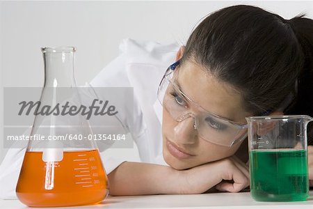 Gros plan d'une jeune femme regardant les gobelets remplis de produits chimiques Gros plan d'une jeune femme regardant les gobelets remplis de produits chimiques