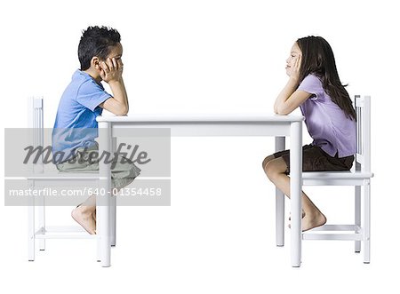 Garçon et fille assise à table avec les mains sur les faces