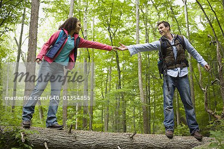 Vue d'angle faible d'un jeune couple, main dans la main et en marchant sur un tronc d'arbre