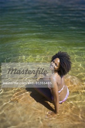 Young woman sitting in water at the edge of a lake