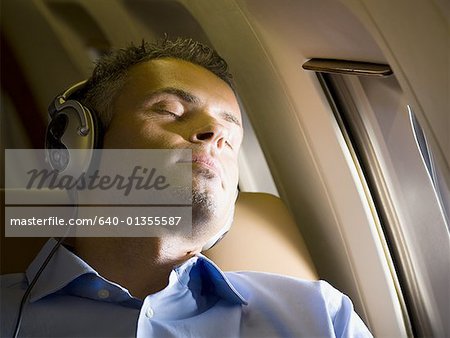 Close-up of a businessman sleeping and  listening to music on headphones in an airplane
