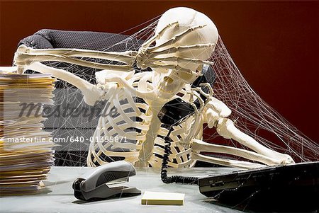 Skeleton sitting at desk talking on telephone with webs and stacks of paperwork