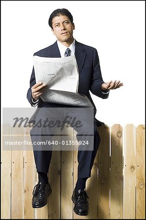 Businessman sitting on fence with newspaper