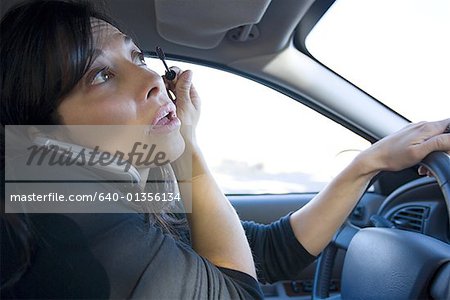 Close-up of a mid adult woman talking on a cell phone and applying eyeliner while driving