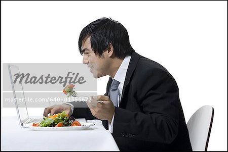 Voir le profil:: un homme d'affaires manger tout en utilisant un ordinateur portable