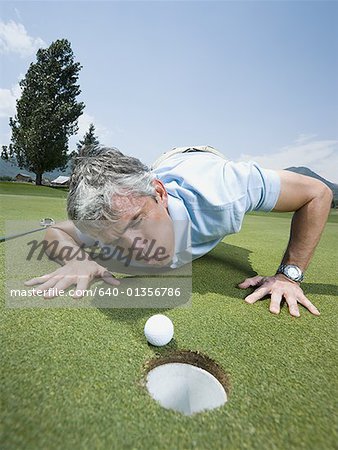 Gros plan d'un homme soufflant une balle de golf vers un trou