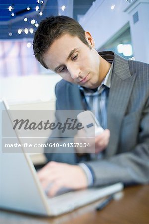 Gros plan d'un homme d'affaires à l'aide d'un téléphone cellulaire en face d'un ordinateur portable