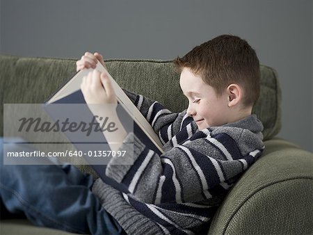 Profile of a boy reading a book on a couch