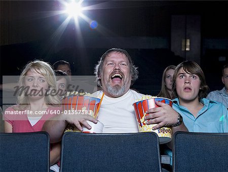 Großer Mann mit einem Eimer Popcorn und Trinken im Kino zwischen paar