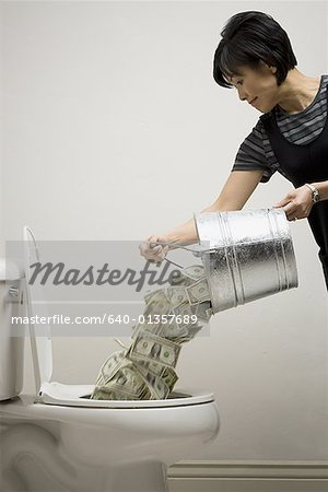 Mid adult woman emptying a bucket of currency notes into a toilet bowl