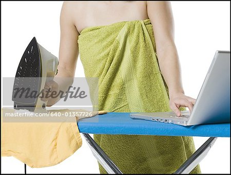 Mid section view of a young woman holding a iron while using a laptop