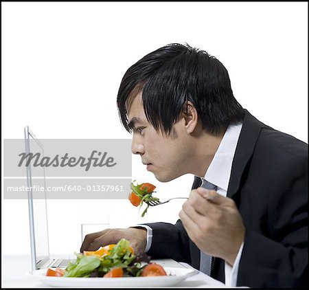 Profile of a businessman eating and using a laptop