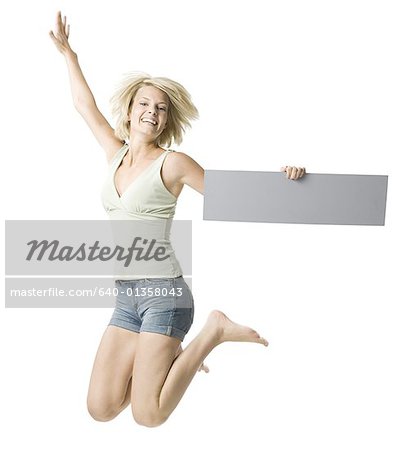 Portrait of a young woman holding a blank sign and jumping