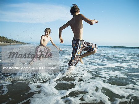 Two boys on beach running in surf