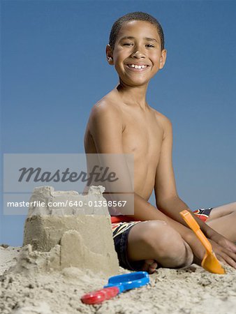 Portrait of a boy sitting beside a sand castle