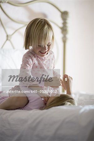 Girl sitting on top of her sister in a bedroom, smiling