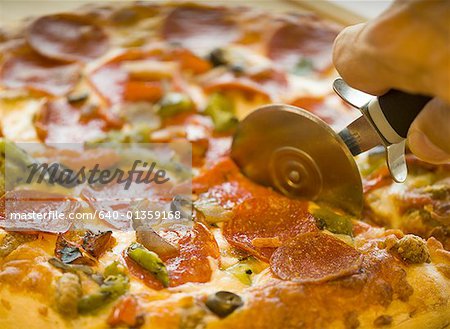 Close-up of a hand cutting a pizza with a pizza cutter