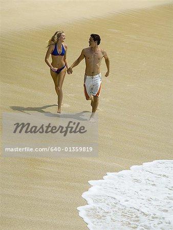 Vue grand angle sur un jeune couple, main dans la main et en cours d'exécution sur la plage