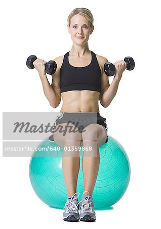 Portrait d'une jeune femme assise sur un ballon de fitness tenant des haltères