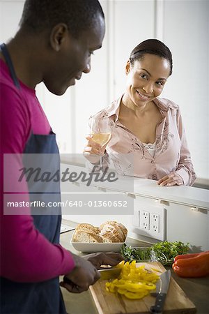 Woman holding a glass of white wine talking to man preparing dinner