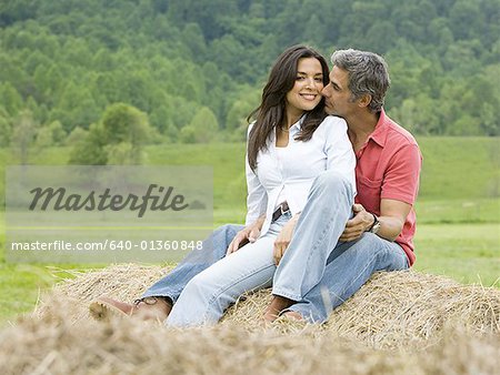 man and a woman sitting on a hay bale