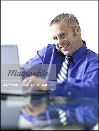 Close-up of a businessman using a laptop and talking on a mobile phone