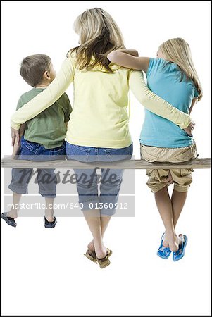 Rückansicht einer Mutter und ihren beiden Kindern sitzen auf einem Holzbrett