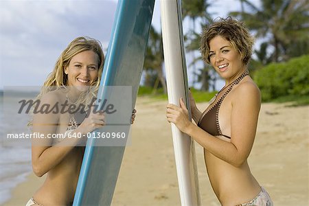 Portrait of two young women holding surfboards and standing on the beach
