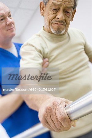 Faible angle vue d'un médecin de sexe masculin aidant un homme senior personnes à mobilité réduite sur un tapis roulant