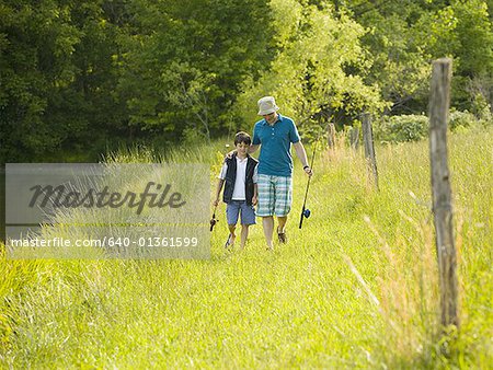 man and his son holding fishing rods and walking in a forest