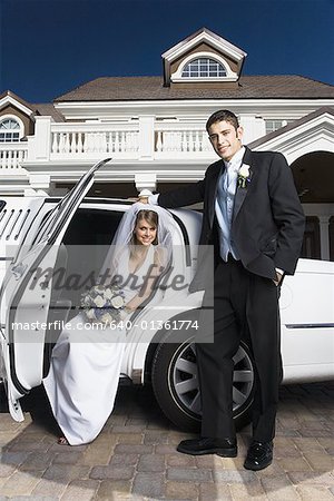 Portrait d'un groom debout avec une épouse assis dans une voiture