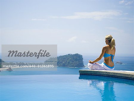 Rear view of a mid adult woman sitting in a lotus position at the poolside and meditating