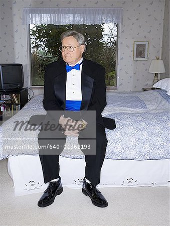 Senior man in tuxedo sitting on bed