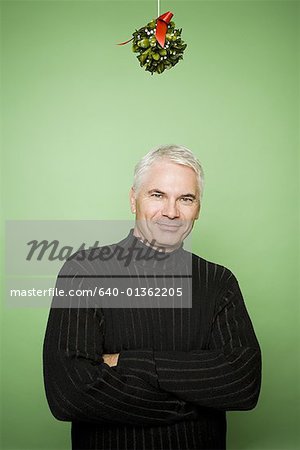 Man with crossed arms under mistletoe at Christmas