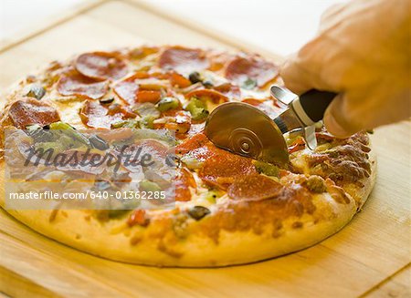 Close-up of a hand cutting a pizza with a pizza cutter