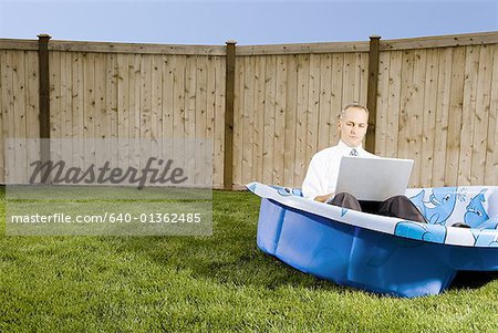 Mid adult man working on a laptop sitting in a wading pool