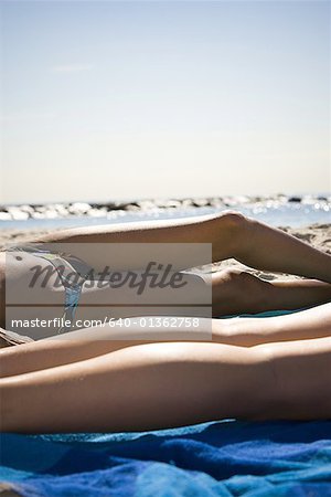 Low section view of two young women sunbathing on the beach
