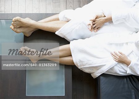 Low section view of an adult couple sitting on a couch with their legs crossed at the ankle