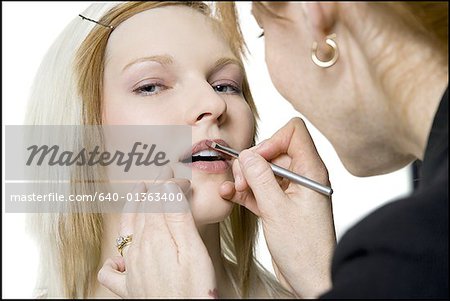 Close-up of a young woman applying lip liner on another young woman's face