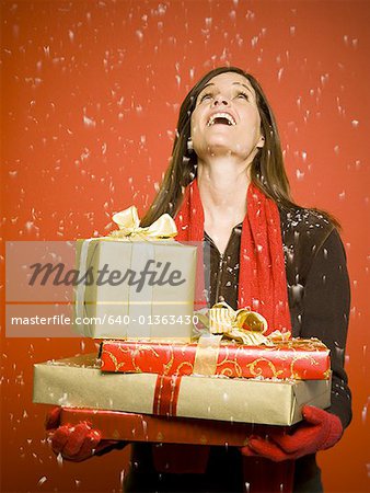 Woman with Christmas gifts looking up at snow