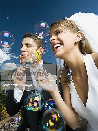 Vue angle faible sur un couple de jeunes mariés bulles avec une baguette à bulles