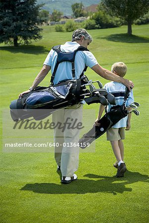 Rear view of a man carrying a golf bag with his son