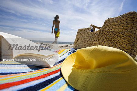 Serviette de plage avec le livre et le sac avec une jeune femme en arrière-plan