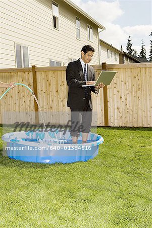 Businessman using a laptop, standing in a wading pool