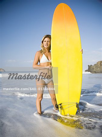 Porträt einer jungen Frau am Strand mit einem Surfbrett stehend