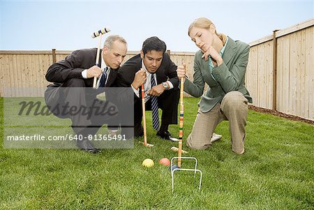 Two businessmen and a businesswoman playing croquet